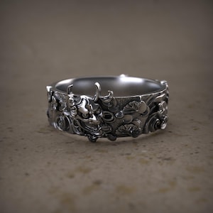 May include: A silver ring with a detailed design featuring a Japanese demon mask and floral patterns.