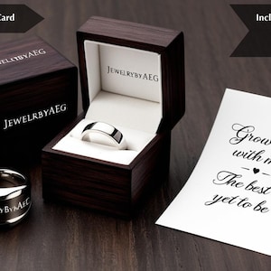 K&ouml;nnte beinhalten: Eine Holzschachtel f&uuml;r einen Ring mit einem silbernen Ring darin. Die Schachtel ist mit den Worten "Jewelry by AEG" graviert. Eine Karte mit dem Text "Grow old with me, The best is yet to be" liegt auf einer Holzoberfl&auml;che.