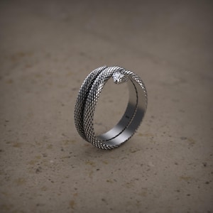 K&ouml;nnte beinhalten: Ein silberner Ring mit einem Schlangendesign. Die Schlange ist um den Ringband gewickelt und ihr Kopf zeigt nach vorne. Der Ring ist aus strukturiertem Metall.
