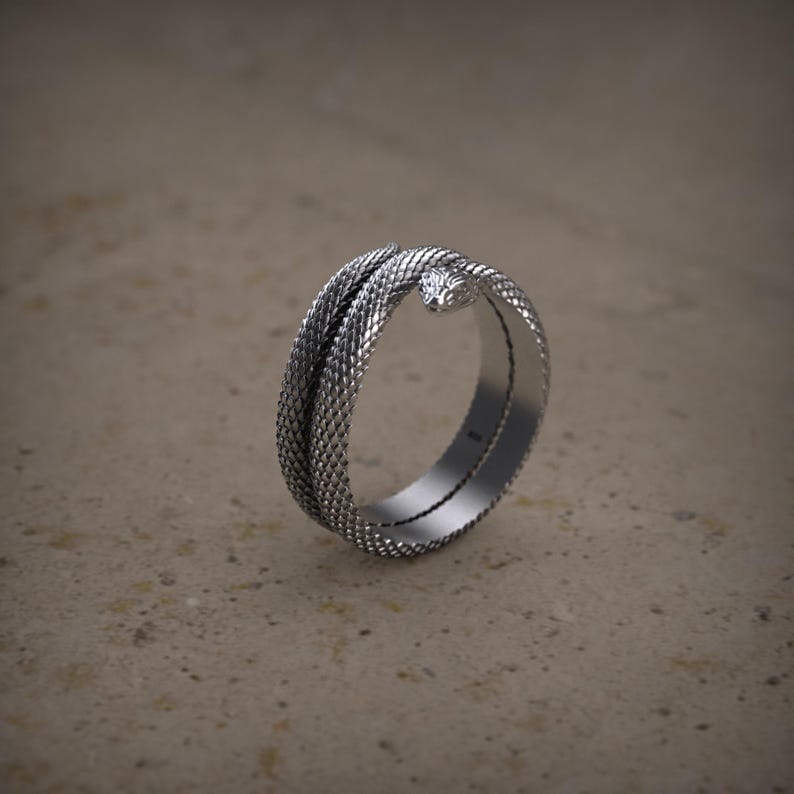 K&ouml;nnte beinhalten: Ein silberner Ring mit einem Schlangendesign. Die Schlange ist um den Ringband gewickelt und ihr Kopf zeigt nach vorne. Der Ring ist aus strukturiertem Metall.