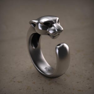 Könnte beinhalten: Ein silberner Ring mit einem geformten Pantherkopf. Der Ring hat eine glatte, polierte Oberfläche und ein einzigartiges offenes Design. Die Zahl "925" ist auf der Innenseite des Rings eingeprägt, was auf die Reinheit des Metalls hinweist.