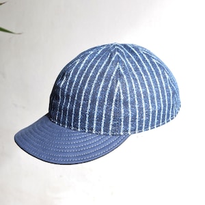 May include: A blue baseball cap with vertical white stripes on the crown and a solid blue brim. The cap has a classic six-panel design and a curved brim. The background is a neutral white, highlighting the cap's details.