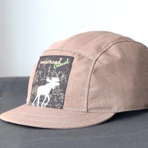 May include: A brown 5-panel cap with a black patch featuring a white moose and the text "smoothhead Casual".