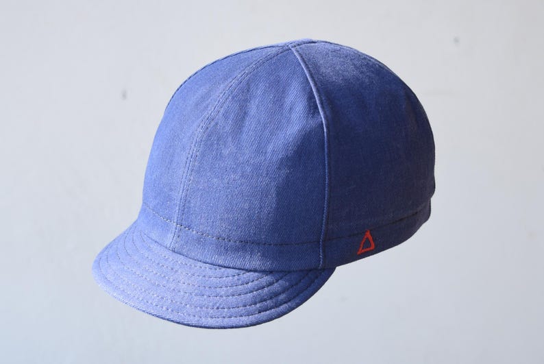 May include: A blue cap with a short brim and a red triangle logo on the side. The cap is made of a textured fabric and has a stitched design. This hat is a stylish accessory.