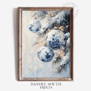 May include: A framed print featuring three blue and white Christmas ornaments with floral and landscape designs. The ornaments hang from snow-covered evergreen branches, with small white lights and a soft, wintery background. The text "DANDEE SOUTH PRINTS" is at the bottom.