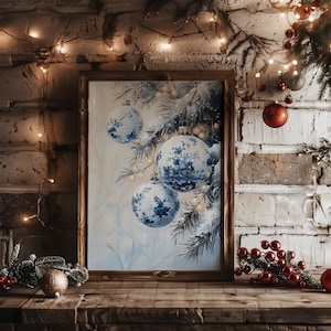 May include: A framed print featuring blue and white Christmas ornaments with a floral design. The artwork is set against a light blue background with pine branches. The frame is made of dark wood, and the scene is set on a wooden surface.