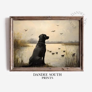 May include: A black Labrador Retriever sits by a lake, watching a flock of ducks swimming in the water. The painting has a vintage feel and is framed in a brown wood frame.