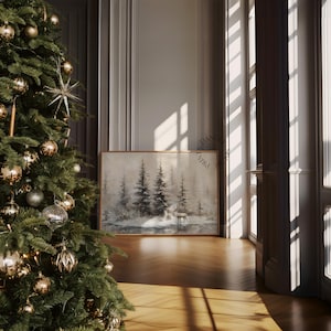 May include: A framed winter landscape painting featuring a forest scene with a deer, displayed in a room with a decorated Christmas tree. The painting has a wooden frame and is set against a neutral wall. The room has a wooden floor and is illuminated by sunlight.