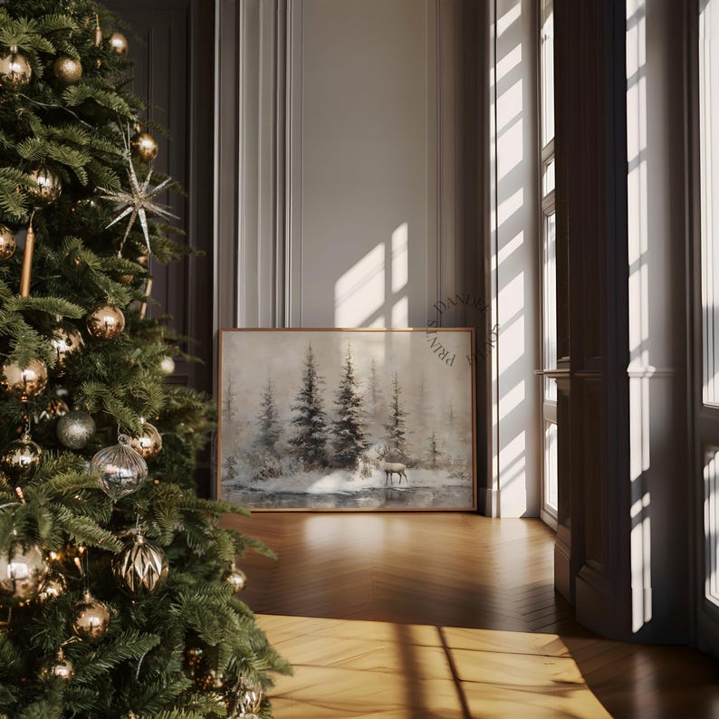 May include: A framed winter landscape painting featuring a forest scene with a deer, displayed in a room with a decorated Christmas tree. The painting has a wooden frame and is set against a neutral wall. The room has a wooden floor and is illuminated by sunlight.