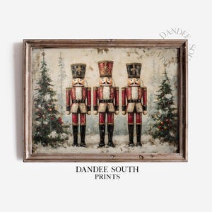 May include: A framed print featuring three toy nutcracker soldiers in red and white uniforms, black boots, and tall hats. The background shows a snowy forest scene with Christmas trees. The print is labeled "DANDEE SOUTH PRINTS".