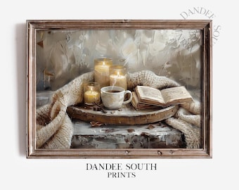 May include: A framed print depicts a cozy scene with lit candles, a cup of coffee, and an open book on a wooden tray. A cream-colored knitted blanket drapes over the tray. The print has the text "DANDEE SOUTH PRINTS".