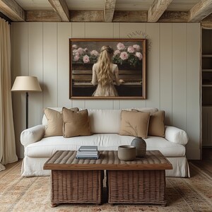 Puede incluir: Un sof&aacute; blanco con almohadas marrones se encuentra en una sala de estar con una mesa de caf&eacute; de madera y una pintura enmarcada de una mujer tocando un piano con flores rosas en el fondo.