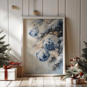 May include: A framed print featuring blue and white Christmas ornaments with a floral design. The ornaments hang from a snowy pine branch. The print is displayed on a wooden surface with gift boxes and a Christmas tree.