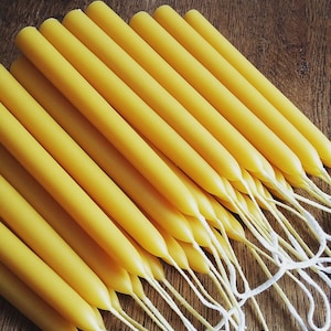 May include: A collection of yellow taper candles with white wicks, arranged diagonally on a wooden surface. The candles are a warm, golden yellow color, and the wicks are neatly bundled together. These candles are suitable for home decor and special occasions.
