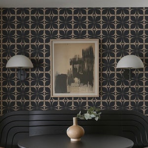 May include: A black dining table with a round top and a pedestal base. Two chairs with woven cane seats and backs are positioned on either side of the table. A black bench with a curved back is behind the table. A vase with greenery sits on the table. The wall behind the table is covered in a black and brown geometric wallpaper. A framed abstract painting hangs on the wall.