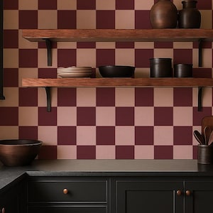 May include: A kitchen scene with a checkered burgundy and beige wall. Wooden shelves hold pottery and bowls. Below, black cabinets with copper knobs and a dark countertop. A wooden cutting board and utensils are visible.