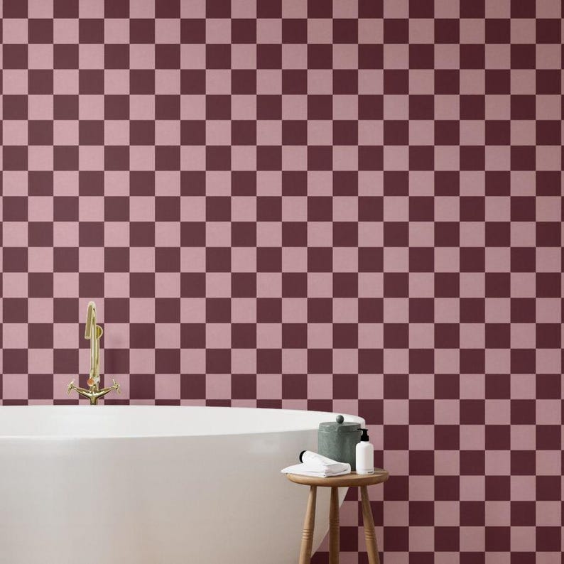 Puede incluir: Una escena de ba&ntilde;o con una ba&ntilde;era blanca, un grifo dorado y un peque&ntilde;o taburete de madera. La pared tiene un patr&oacute;n de tablero de ajedrez de cuadrados burdeos oscuros y claros. Un peque&ntilde;o recipiente, una botella y una toalla enrollada est&aacute;n en el taburete.