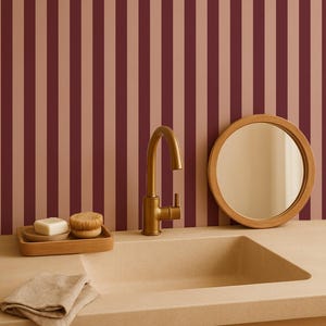 May include: A bathroom sink with a gold faucet, round mirror, and soap dish. The sink is beige, and the background has vertical stripes in burgundy and beige. A folded beige towel rests on the counter.