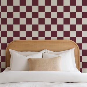 May include: A bed with a white headboard and white bedding. The headboard is made of wood and has a rounded top. The wall behind the bed is covered in a checkerboard pattern wallpaper with burgundy and white squares.