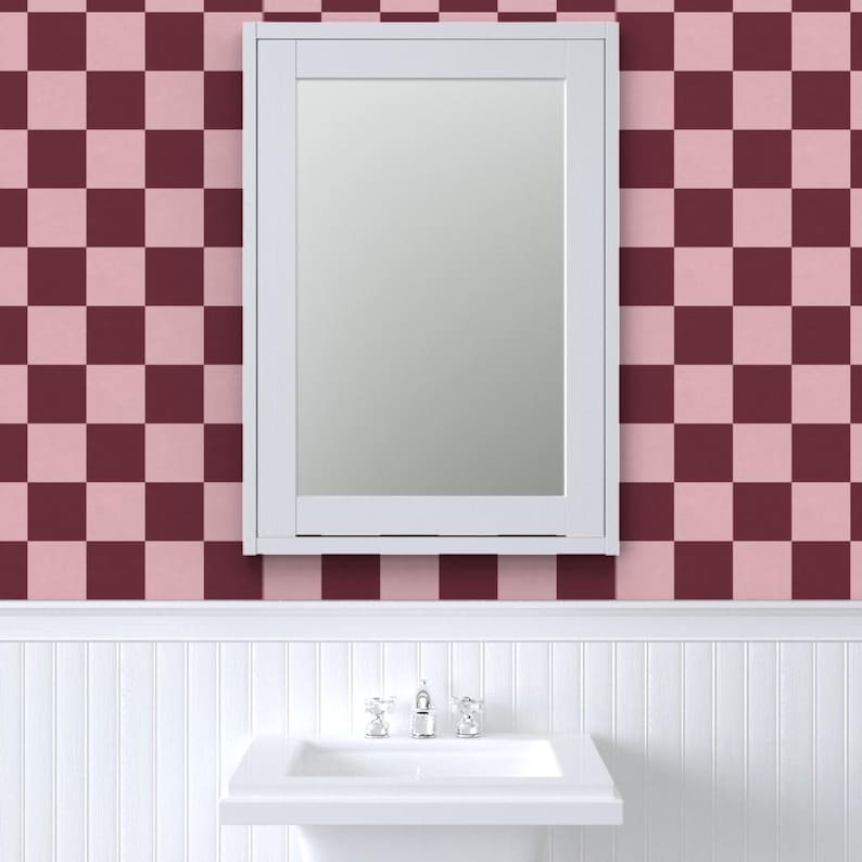 Puede incluir: Un espejo con marco blanco cuelga de una pared con un patr&oacute;n de cuadros en tonos rosa y burdeos. Debajo del espejo hay un lavabo blanco con un grifo cromado, sobre una pared con paneles blancos.