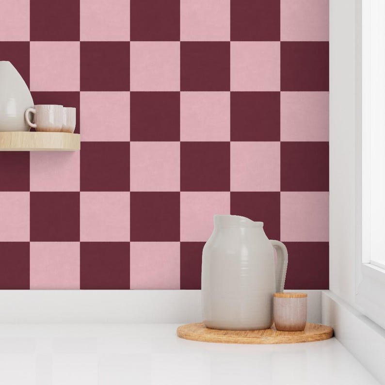 Puede incluir: Un patr&oacute;n de tablero de ajedrez en tonos rosa y burdeos cubre la pared. Una jarra blanca, una peque&ntilde;a taza de madera y una bandeja de madera se encuentran sobre una superficie blanca. Una peque&ntilde;a estanter&iacute;a contiene un jarr&oacute;n blanco y dos tazas peque&ntilde;as.