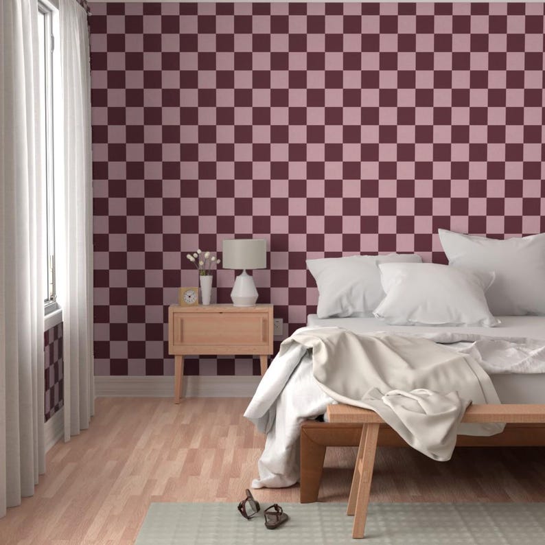 Puede incluir: Un dormitorio con una pared a cuadros burdeos y rosa. La habitaci&oacute;n tiene una mesita de noche de madera con una l&aacute;mpara, una cama con ropa de cama blanca y un banco de madera al pie de la cama. El suelo es de madera clara y se ve una ventana con cortinas blancas.