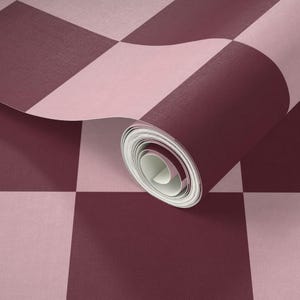 Puede incluir: Un rollo de papel pintado con un dise&ntilde;o de tablero de ajedrez en tonos burdeos y rosa claro. El papel est&aacute; parcialmente desenrollado, revelando el interior enrollado. El dise&ntilde;o es un patr&oacute;n geom&eacute;trico cl&aacute;sico.