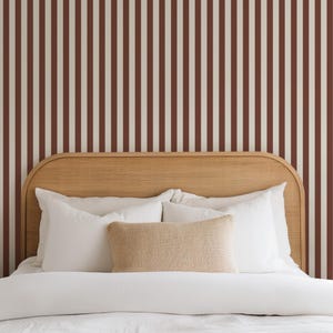 May include: A bedroom scene featuring a bed with white bedding, pillows, and a woven headboard. The wall behind the bed has a vertical striped pattern in burgundy and cream.