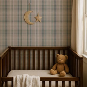 May include: A wooden crib with a brown teddy bear and a white blanket. The crib is set against a plaid wallpaper in shades of blue, gray, and beige. A gold crescent moon and star hang on the wall above the crib.