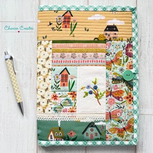 May include: A green and white patchwork quilt with a floral and house design. The quilt has a green gingham border and a white lace trim. The quilt is quilted with a simple straight stitch pattern. The quilt is labeled "Charisse Creates" in the top left corner.