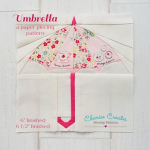 Puede incluir: Un patrón de patchwork para un bloque de colcha en forma de paraguas. El bloque tiene 15,24 cm de lado una vez terminado y representa un paraguas rosa con estampado floral y un mango rosa. El texto "Umbrella", "a paper piecing pattern", "Vintage Buttons", "Ranais Jescu" y "Charise Creates Sewing Patterns" está incluido en la imagen.
