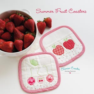 May include: Two square fabric coasters with red and white gingham trim. One coaster features a quilted apple design with text, and the other displays three cherry motifs. A white bowl filled with fresh strawberries sits nearby. Text reads Summer Fruit Coasters.