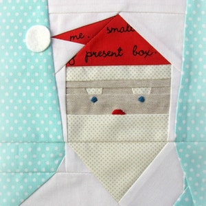 May include: A paper piecing pattern for a Santa stocking. The pattern is made up of different fabric pieces, including red, white, and beige. The pattern includes the text "Santa Stocking" and "a paper piecing pattern".