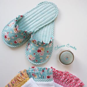 May include: A pair of quilted, floral-print slippers with a ruffled edge. The slippers are light blue with a floral pattern and a gingham trim. The slippers are approximately 10 inches long.