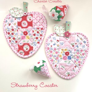 Op de afbeelding: Twee gewatteerde aardbeivormige onderzetters met patchworkstof in roze, rood en wit met bloemen- en ruitpatronen, elk bekroond met een groen blaadje en een kleine bloemknop. Twee kleine gevulde aardbei-ornamenten zijn ook inbegrepen.