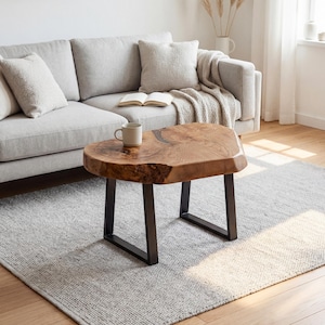 May include: A live edge coffee table with a natural wood grain finish and black metal legs. The table is approximately 30 inches long, 20 inches wide, and 16 inches high. A mug sits on the table's surface, near a light gray sofa and rug.