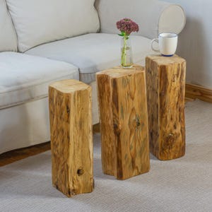 Könnte beinhalten: Drei rustikale Beistelltische aus Holz mit natürlicher Maserung. Auf einem Tisch steht eine kleine Vase mit lila Blumen, auf einem anderen eine weiße Tasse mit blauem Rand. Die Tische stehen auf einem hellgrauen Teppich. Höhe ca. 40 cm.