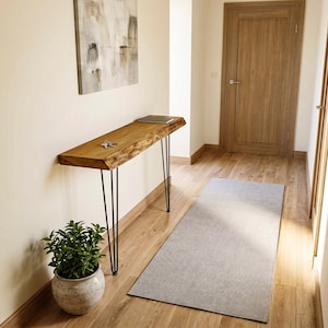Può includere: Un tavolo consolle stretto caratterizzato da un piano in legno naturale con bordo grezzo e finitura marrone caldo, sostenuto da quattro sottili gambe a forcina in metallo nero. Un mazzo di chiavi argentate poggia sul piano in legno nel corridoio.