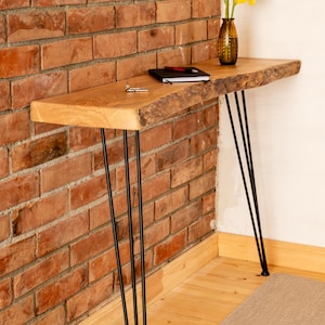 Puede incluir: Consola de madera con patas de horquilla negras. La mesa tiene un borde natural. Un jarrón con flores amarillas, un cuaderno y llaves están sobre la mesa, frente a una pared de ladrillos rojos.