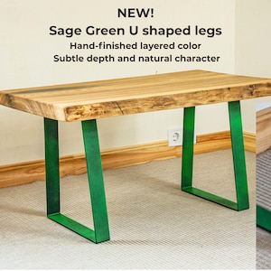 Sage green metal table legs in handmade layered finish with subtle patina effect, unique color option for live edge solid ash wood coffee table, Scandinavian style natural furniture detail, green U shaped steel legs close up showing textured matte surface and artisan craftsmanship, modern organic interior design accent