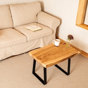 Può includere: Tavolino da caffè rettangolare in legno con finitura a venature naturali. Il tavolo ha gambe in metallo nero ed è lungo circa 91 cm e largo 51 cm. Una tazza bianca con bordo blu è appoggiata sul tavolo.