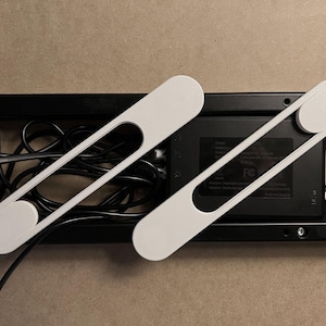 May include: Two white cable organizers with an oval shape at each end and a central cutout, resting on a black cable management tray. The tray holds various black cables and a black power supply unit.