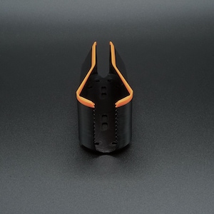 May include: A black and orange bottle holder. The holder is cylindrical with an open top and a curved orange trim. The holder has a series of small holes and is set against a dark background.