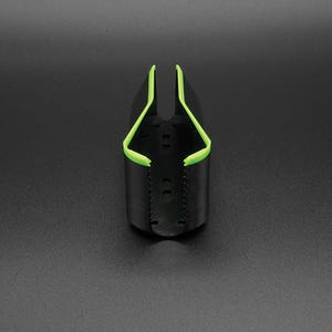 May include: A black, cylindrical object with a bright green trim. The object has a curved, open top and a series of small holes along the sides. The green trim outlines the top edges, creating a contrasting design. The object is set against a dark background.