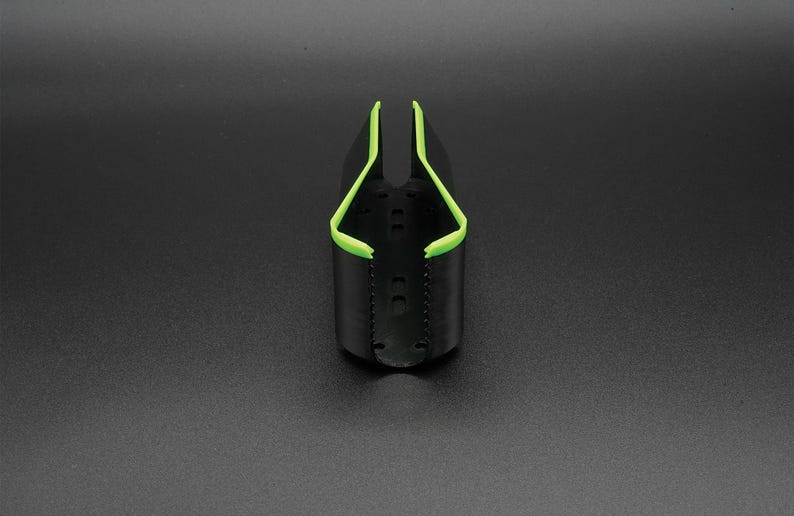 May include: A black, cylindrical object with a bright green trim. The object has a curved, open top and a series of small holes along the sides. The green trim outlines the top edges, creating a contrasting design. The object is set against a dark background.