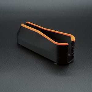May include: A black rectangular object with orange trim. The object has a U-shaped opening and appears to be made of a solid material. The orange trim lines the top edges of the object.
