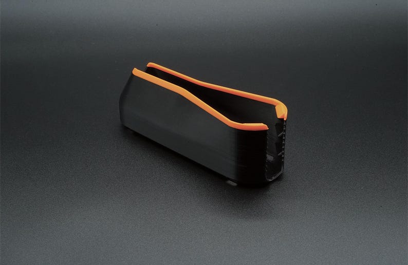 May include: A black rectangular object with orange trim. The object has a U-shaped opening and appears to be made of a solid material. The orange trim lines the top edges of the object.
