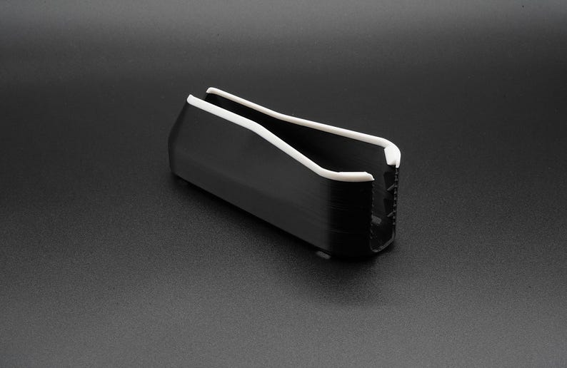 May include: A black, rectangular object with a white, curved top and interior. The object is set against a dark gray background. The design is modern and minimalist.