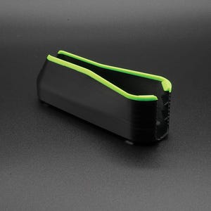 May include: A black rectangular object with a neon green trim along the top edges. The object has a ridged texture on one end and is set against a dark gray background.