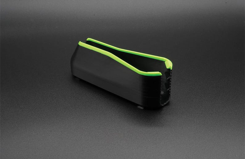 May include: A black rectangular object with a neon green trim along the top edges. The object has a ridged texture on one end and is set against a dark gray background.